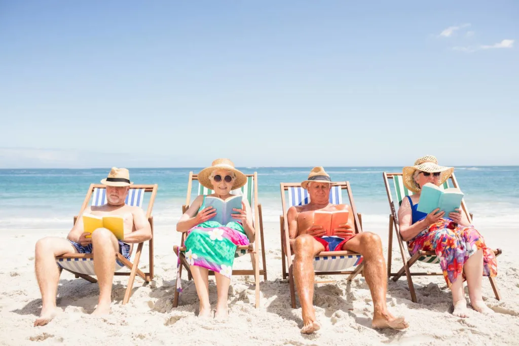 Senior friends reading books on beach chair on reading retreat